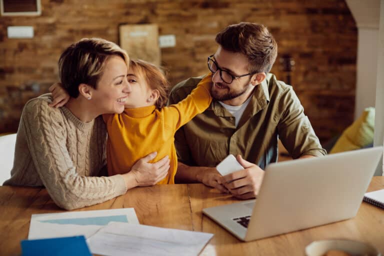 Happy parents having fun with their small daughter who is embracing and kissing them at home.