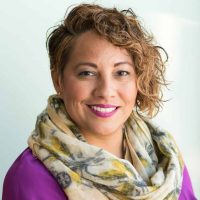 Smiling woman in a purple dress and scarf holding a tablet indoors.