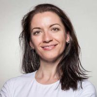 Portrait of a confident woman smiling with arms crossed, wearing a white t-shirt on a gray background.